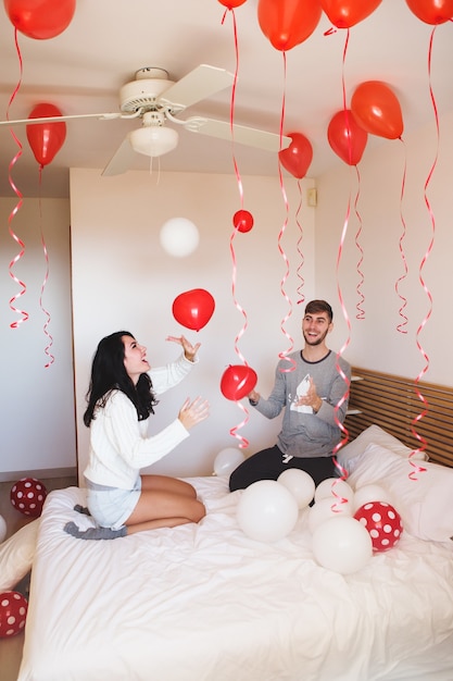 Man glimlachend terwijl zijn vriendin kijkt naar de kamer vol met rode ballonnen