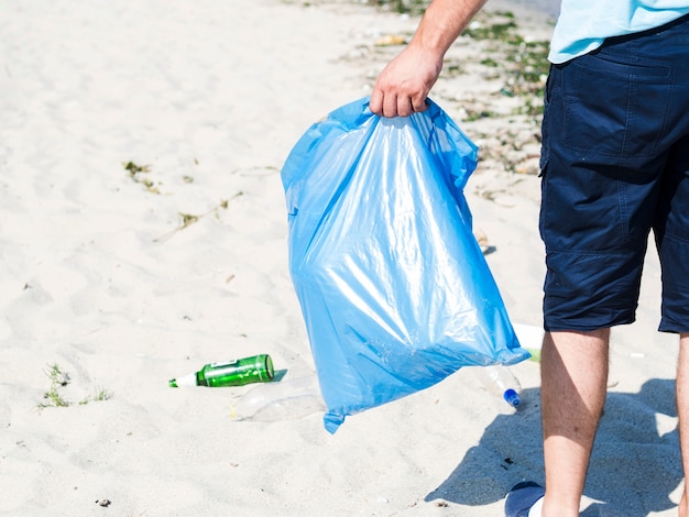 Man hand die blauwe vuilniszak op strand draagt