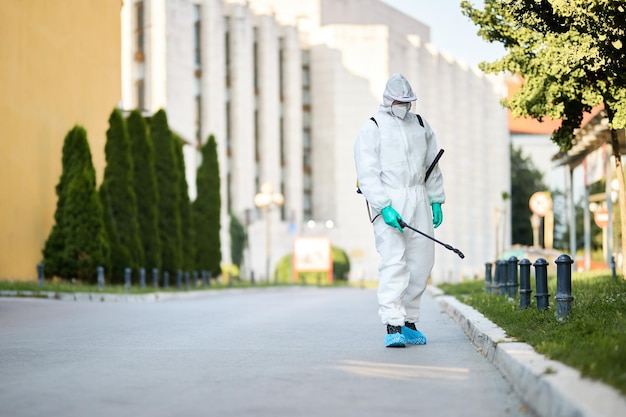 Man in beschermend pak die stadsstraten desinfecteert tijdens pandemie van het coronavirus