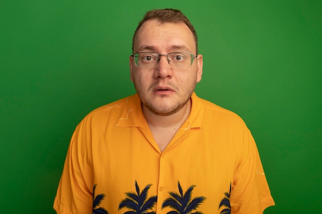 Gratis foto man in bril en hawaiiaans overhemd die verward en zeer angstig over groene muur staan