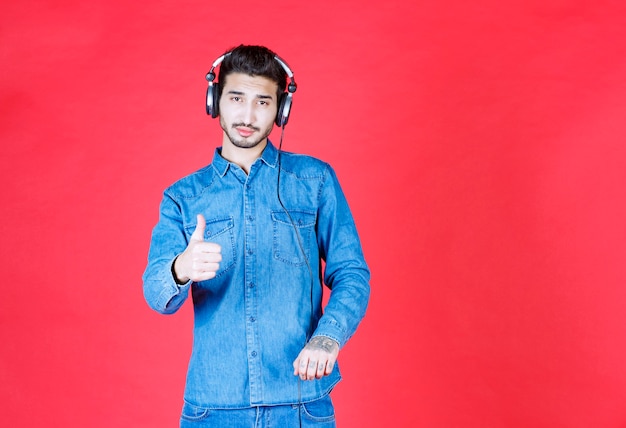 Man in denim shirt met een koptelefoon en een positief handteken.