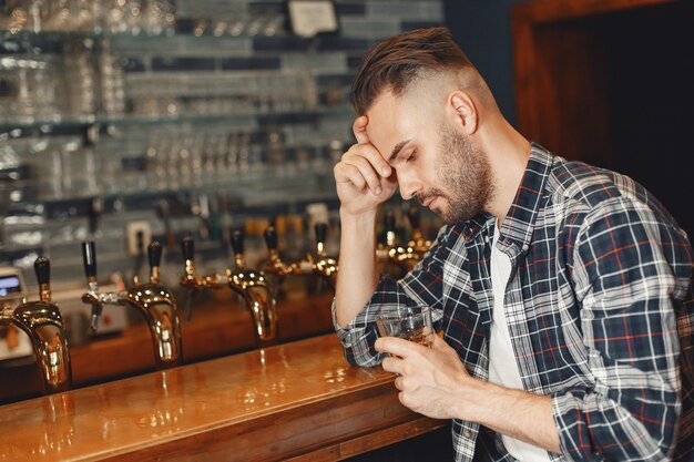 Man in een overhemd heeft een glas in zijn handen. Guy zit aan de bar en houdt zijn hoofd vast.