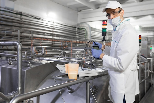 Man in een witte jashandschoenen en een masker staat in de buurt van de productielijn en houdt een tester met draden vast in de zuivelfabriek De inspecteur voert de controle uit in de kaasfabriek