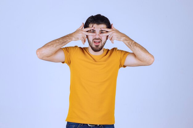 Man in geel shirt kijkt door zijn vingers.