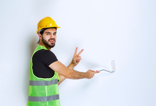 Man in gele helm die de muur schildert.