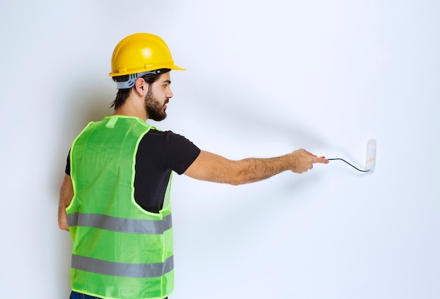 Man in gele helm die de muur schildert.