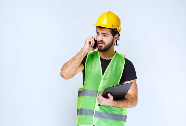 Man in gele helm praten aan de telefoon.