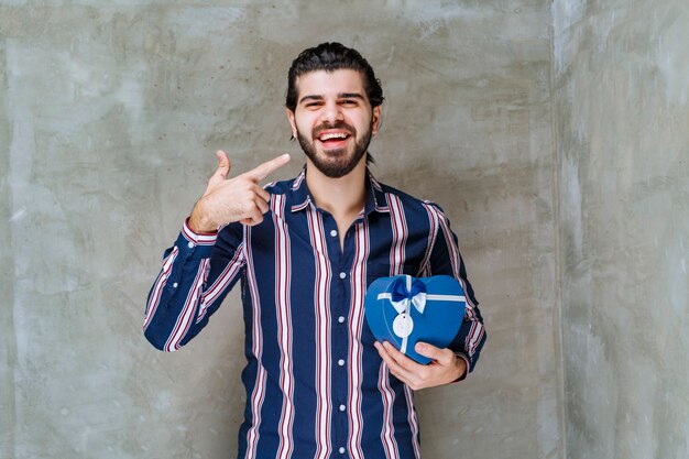 Man in gestreept shirt met een blauwe geschenkdoos in de vorm van een hart