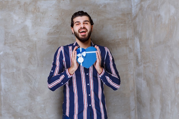 Man in gestreept shirt met een blauwe geschenkdoos in de vorm van een hart