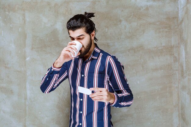 Man in gestreept shirt met een kopje drinken terwijl hij een visitekaartje vasthoudt