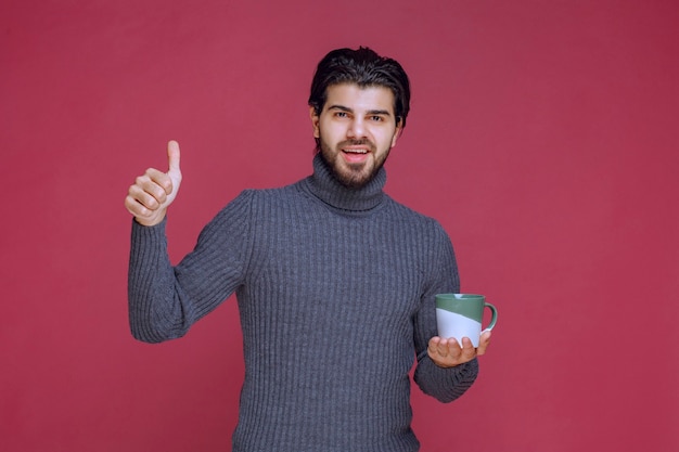 Man in grijze trui met een koffiemok en genietend van de smaak.