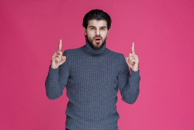 Man in grijze trui om iets te wijzen of iemand te introduceren die wijsvinger gebruikt.