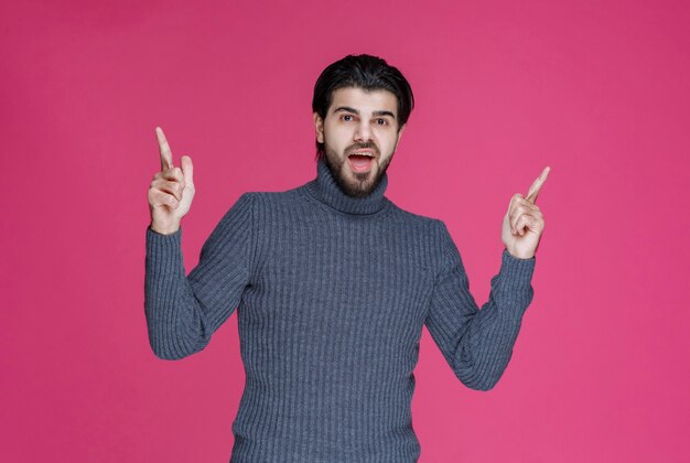 Man in grijze trui om iets te wijzen of iemand te introduceren die wijsvinger gebruikt.