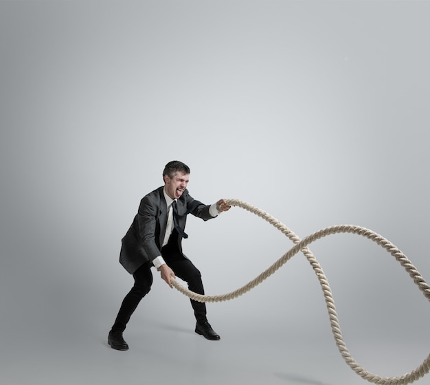 Man in office kleding training met touwen op een grijze achtergrond.