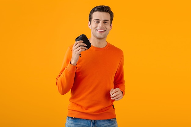 man in oranje trui met draadloze luidspreker gelukkig luisteren naar muziek plezier kleurrijke stijl gelukkige stemming geïsoleerd op geel