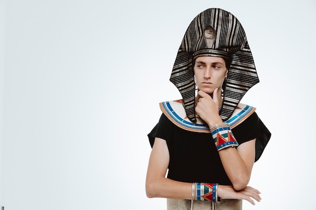 Gratis foto man in oud egyptisch kostuum opzij kijkend met peinzende uitdrukking denkend met de hand op zijn kin op wit