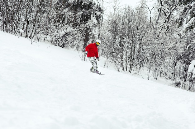 Man in rode ski-jack daalt op de snowboard langs het bos