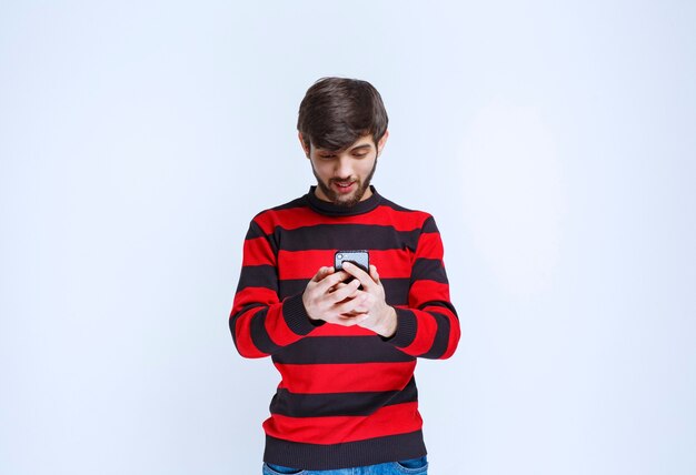 Man in rood gestreept shirt chatten of sms'en op zijn smartphone.