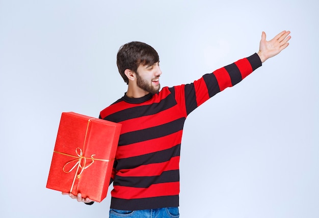 Man in rood gestreept shirt die een rode geschenkdoos vasthoudt en iemand roept om het te bezorgen.