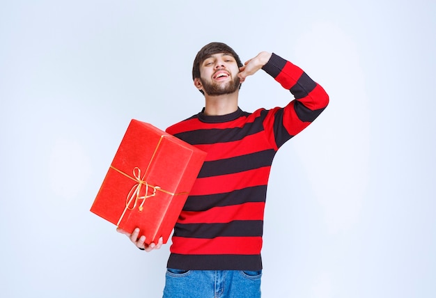 Man in rood gestreept shirt die een rode geschenkdoos vasthoudt en iemand roept om het te bezorgen.