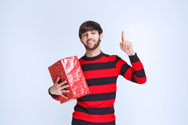 Man in rood gestreept shirt die een rode geschenkdoos vasthoudt en iemand roept om het te bezorgen.