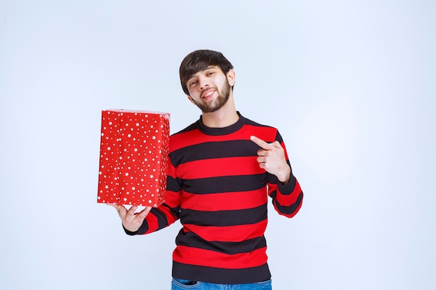 Man in rood gestreept shirt die een rode geschenkdoos vasthoudt en promoot.
