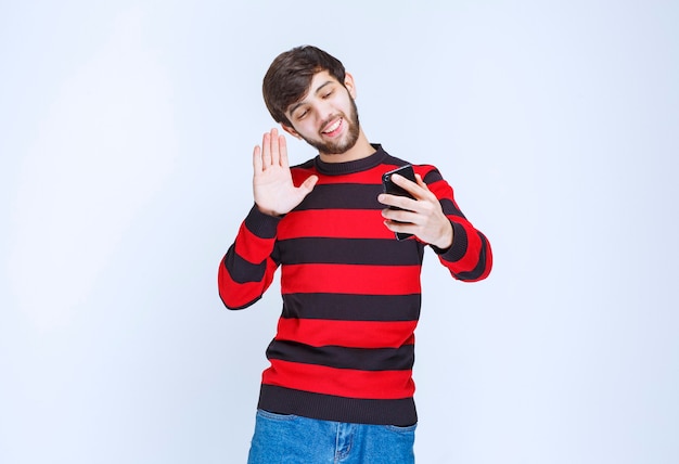 Man in rood gestreept shirt die telefoon vasthoudt en zijn selfie in energieke poses neemt.