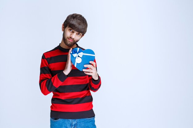 Man in rood gestreept shirt met een blauwe geschenkdoos in de vorm van een hart.