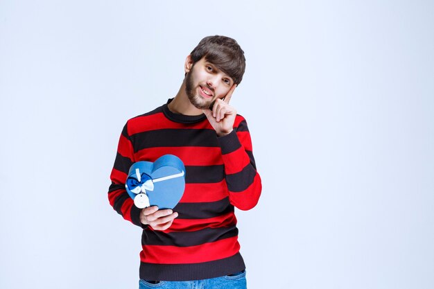 Man in rood gestreept shirt met een blauwe hartvormige geschenkdoos en ziet er attent uit of alsof hij een goed idee heeft.