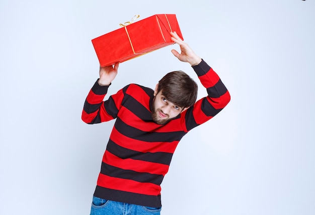 Man in rood gestreept shirt met een rode geschenkdoos, afleveren en presenteren