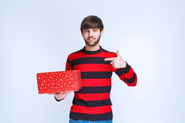 Man in rood gestreept shirt met een rode geschenkdoos en belt iemand om het te presenteren.