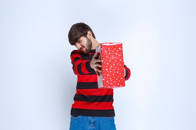 Man in rood gestreept shirt met een rode geschenkdoos en biedt het aan