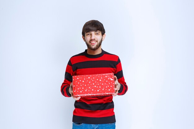 Man in rood gestreept shirt met een rode geschenkdoos en biedt het aan