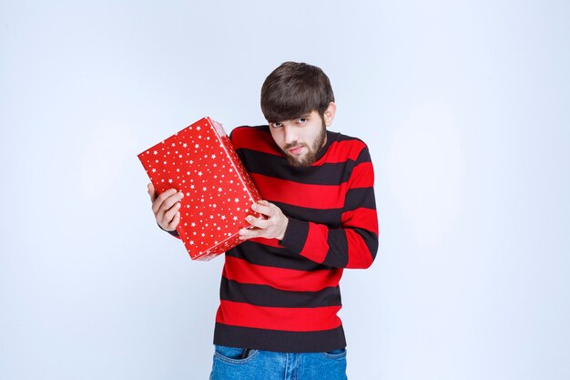 Man in rood gestreept shirt met een rode geschenkdoos en biedt het aan