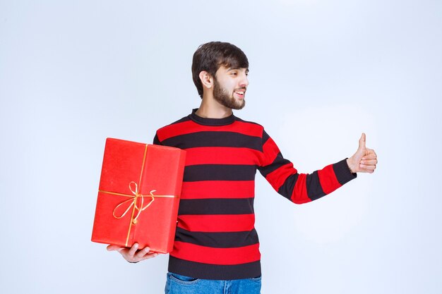 Man in rood gestreept shirt met een rode geschenkdoos en voelt zich krachtig en positief.