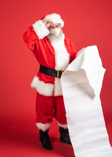 Man in santakostuum met medische masker met geschenkenlijst