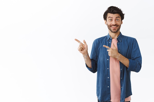 man in shirt, roze t-shirt, vrolijk en geamuseerd glimlachend, wijzend naar de linkerbovenhoek, advies geven, goede promo aanbevelen