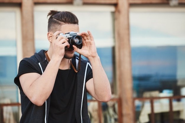 man in trendy outfit fotograferen op straat, kijkend door de camera