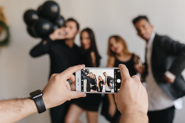 Man in trendy polshorloge met behulp van smartpone om foto te nemen op feestje