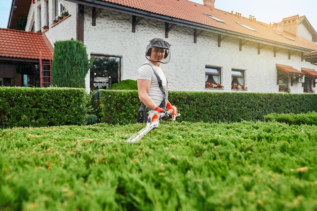 Gratis foto man in uniforme bril en handschoenen snoeit struiken in de tuin