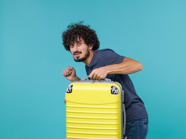 man in vakantie in blauw t-shirt die stilletjes weggaat met zijn koffer op blauw