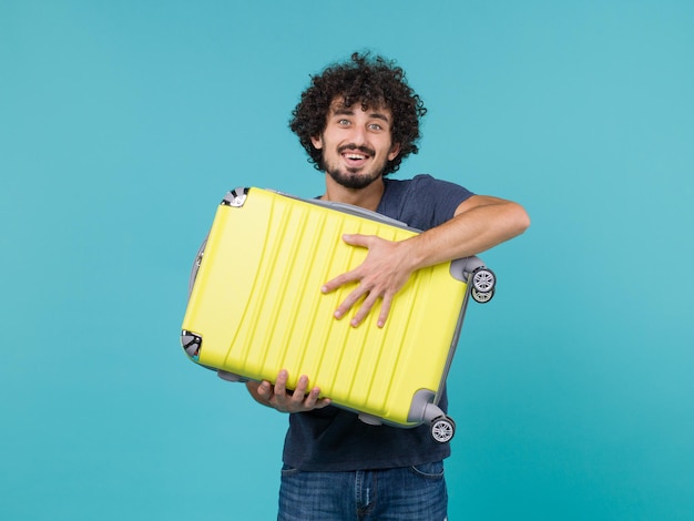 man in vakantie met grote gele koffer op blauw