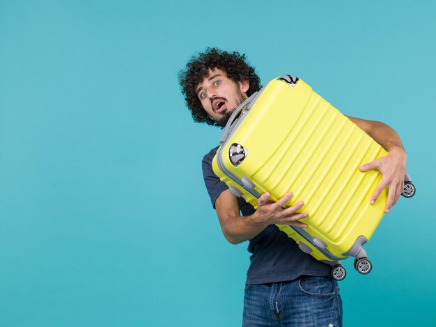 man in vakantie met grote gele koffer op blauw