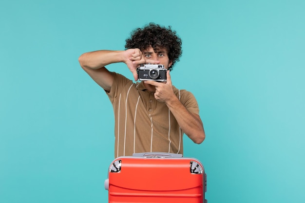 man in vakantie met grote rode koffer die foto's maakt met camera op blauw
