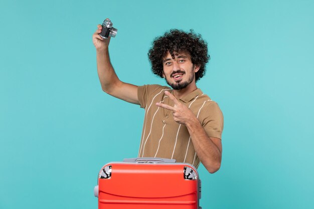 man in vakantie met grote rode koffer die foto's maakt met camera op blauw