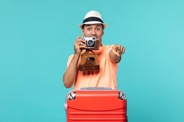 man in vakantie met zijn rode koffer die foto's maakt met camera op blauw