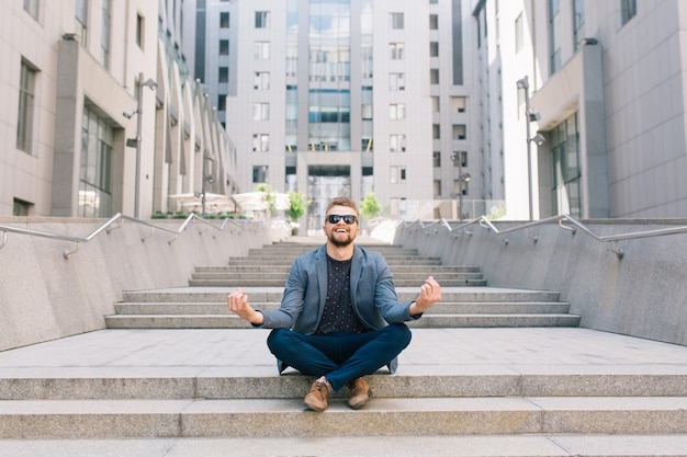 Man in zonnebril zittend op betonnen trap in meditatie pose