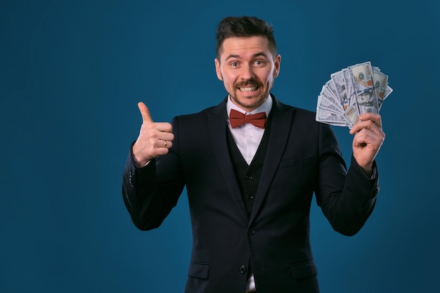 Man in zwart pak en rode vlinderdas toont een fan van honderd-dollarbiljetten die zich voordeed op de achterkant van de blauwe studio...