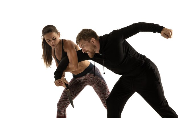 Man in zwarte outfit en atletische blanke vrouw vechten op witte studio achtergrond. Zelfverdediging, rechten, gelijkheid van vrouwen. Tegengaan van huiselijk geweld of diefstal op straat.