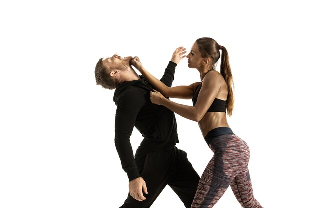 Man in zwarte outfit en atletische blanke vrouw vechten op witte studio achtergrond. Zelfverdediging, rechten, gelijkheid van vrouwen. Tegengaan van huiselijk geweld of diefstal op straat.